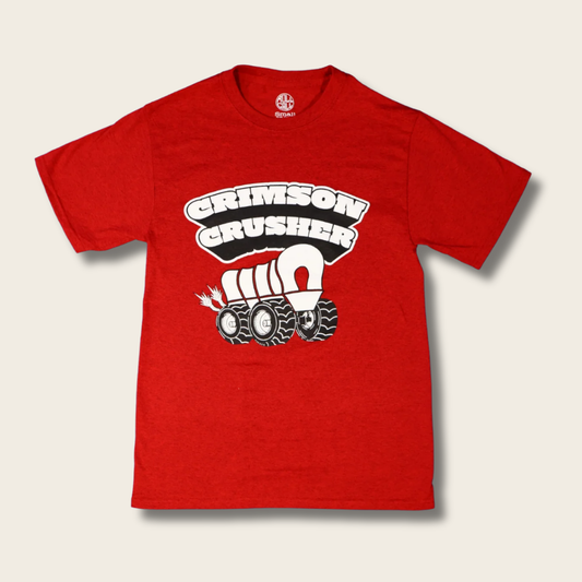 A red short-sleeve crewneck t-shirt featuring a graphic of a tractor pulling a covered wagon with the text 'CRIMSON CRUSHER' above it, displayed on a light beige background.