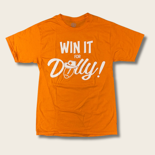 An orange short-sleeve t-shirt with a white graphic print reading 'WIN IT FOR Dolly!' with a football and cowboy hat illustration, displayed on a light beige background.