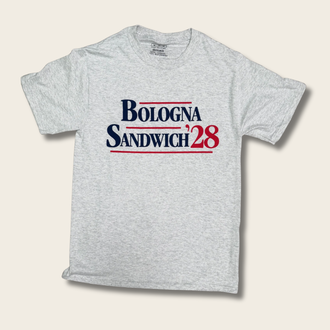 A light heather gray t-shirt featuring the text 'BOLOGNA SANDWICH'28' printed on the chest in navy blue and red with thin red horizontal lines, displayed against a light beige background.