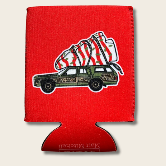 A red can cooler sleeve featuring a graphic of a green wood-paneled station wagon carrying a striped Christmas tree, shown on a light beige background.