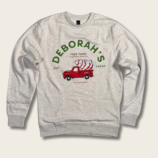 A light heather gray crewneck sweatshirt featuring a vintage-style graphic of a red pickup truck carrying a stack of Christmas trees, with green text reading 'DEBORAH'S TREE FARM' and 'CUT FRESH'.