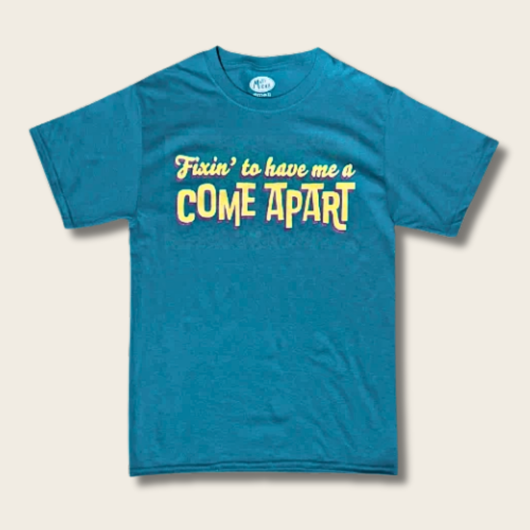 A teal blue short-sleeve t-shirt with a graphic text print reading 'Fixin' to have me a COME APART' in yellow and white, displayed flat against a light beige background.