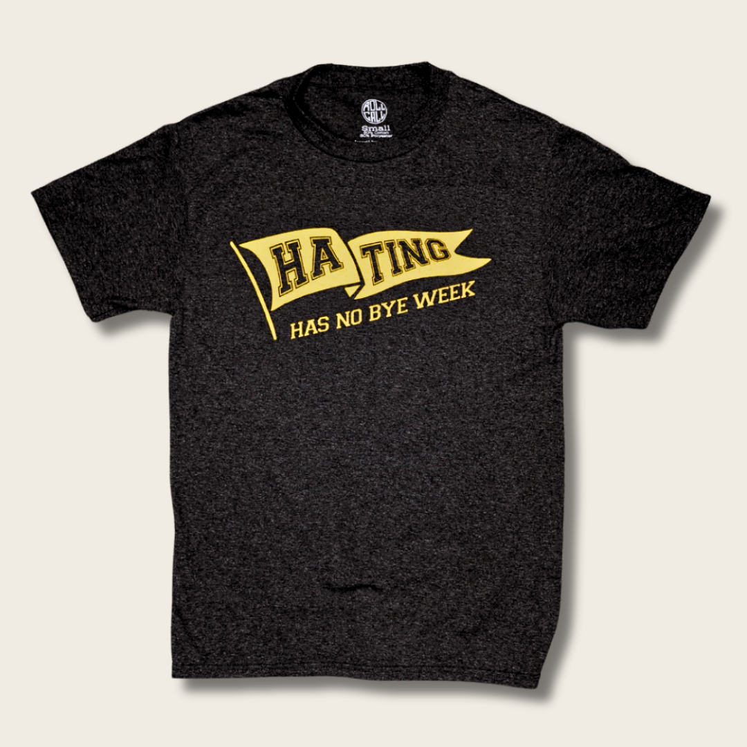 A black t-shirt with a yellow graphic on the front that reads 'HA TING HAS NO BYE WEEK' inside a banner design, displayed on a light beige background.