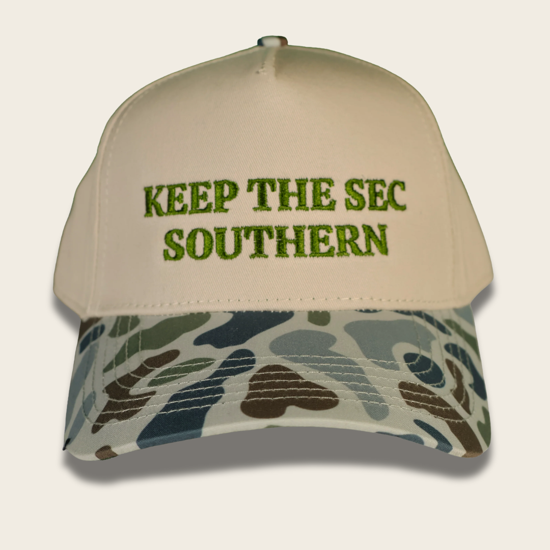 A beige baseball cap with green embroidered text reading 'KEEP THE SEC SOUTHERN' on the front, and a camouflage-patterned visor in shades of green, brown, and gray, shown on a light beige background.