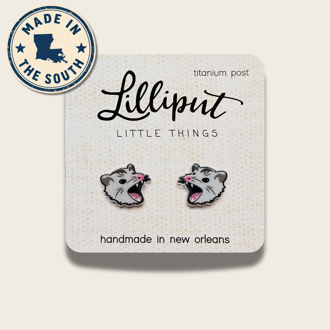 A pair of small animal stud earrings mounted on a white display card. The card reads 'Lilliput LITTLE THINGS' and 'handmade in new orleans,' with ' titanium post' near the top right.