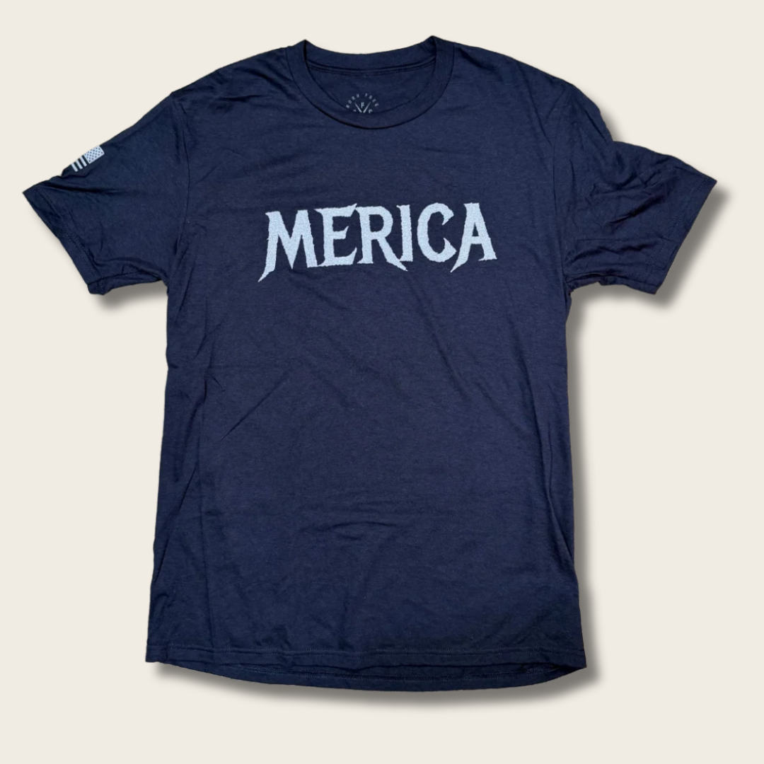 A navy blue short-sleeve t-shirt with the word 'MERICA' printed in a stylized white font across the chest, displayed flat against a light beige background.