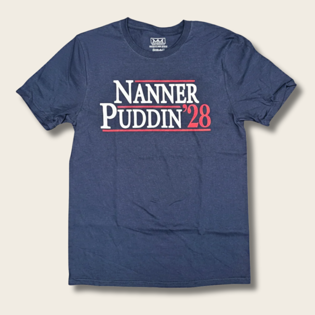 A navy blue short-sleeve t-shirt with a graphic print reading 'NANNER PUDDIN'28' in white and red text across the chest, displayed flat against a light beige background.