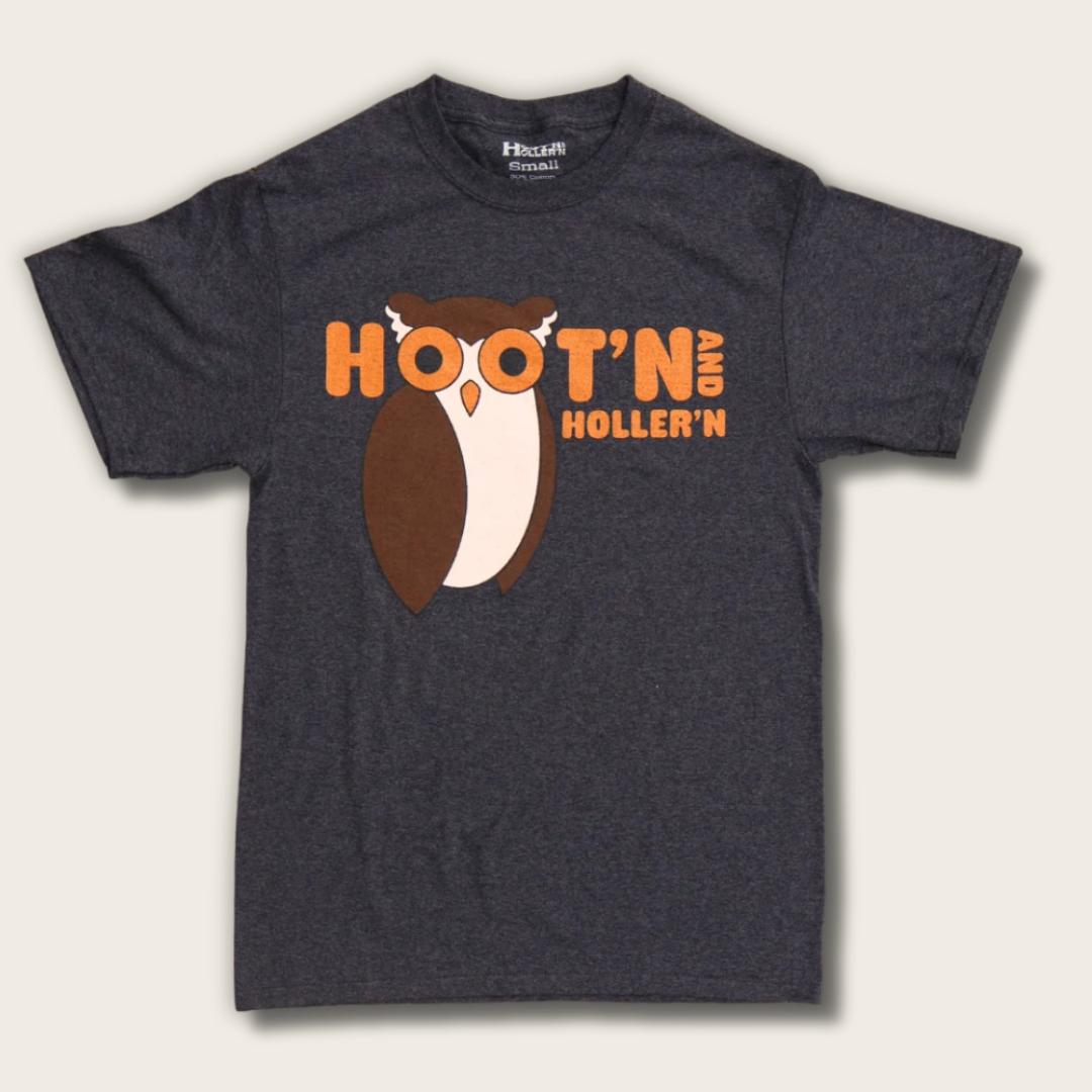 A dark heather gray t-shirt featuring a graphic of a brown and white owl with orange glasses and the text 'HOOT'N' HOLLER'N' in orange, displayed against a light beige background.