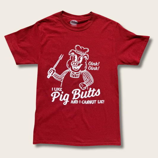 A red short-sleeve crewneck t-shirt featuring a white graphic of a cartoon pig wearing a chef's hat and holding a fork, with the text 'I LIKE Pig Butts AND I CANNOT LIE!' and 'Oink! Oink!'.