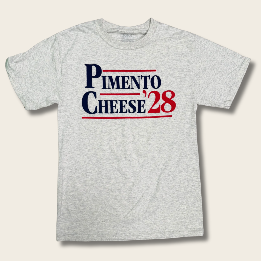 A light heather gray crewneck t-shirt featuring a 'PIMENTO CHEESE '28' graphic on the chest in navy blue and red, displayed against a light beige background.