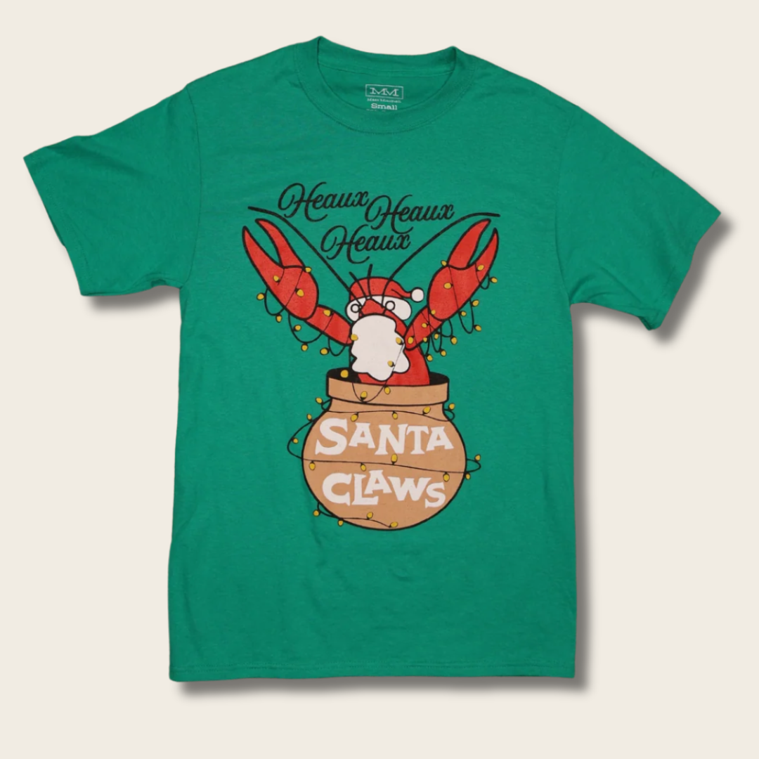 A green short-sleeve crewneck t-shirt featuring a cartoon graphic of a lobster dressed as Santa Claus with its claws raised, emerging from a sack labeled 'Santa Claws' and wrapped in holiday lights. The text 'Heavens Heavens' is written above in black cursive.