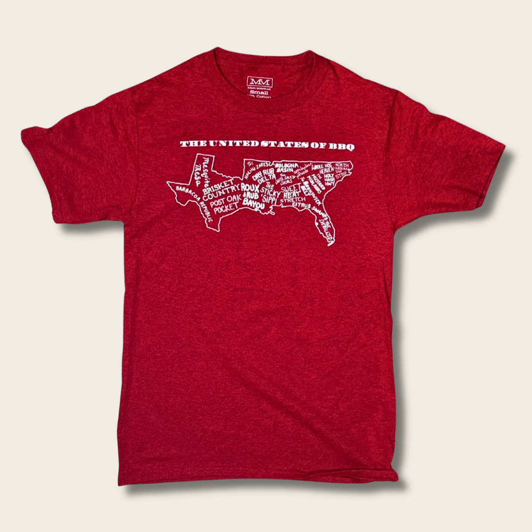 A heather red short-sleeve t-shirt with a white graphic of the United States map filled with BBQ terms, labeled 'THE UNITED STATES OF BBQ' above it, shown on a light beige background.