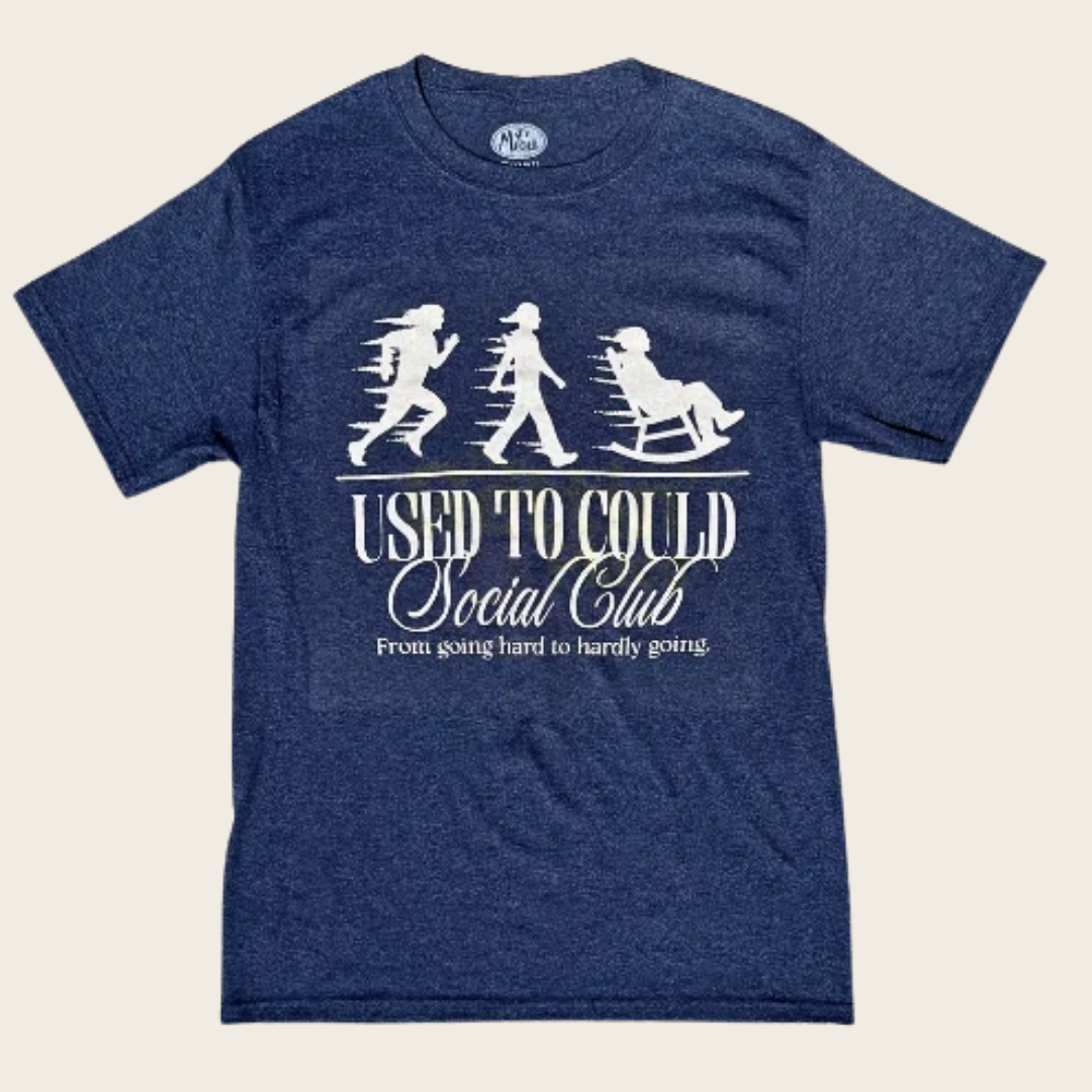 A heather navy blue t-shirt with a white graphic print on the front showing the evolution of sitting down, with the text 'USED TO COULD Social Club' and 'From going hard to hardly going.'.