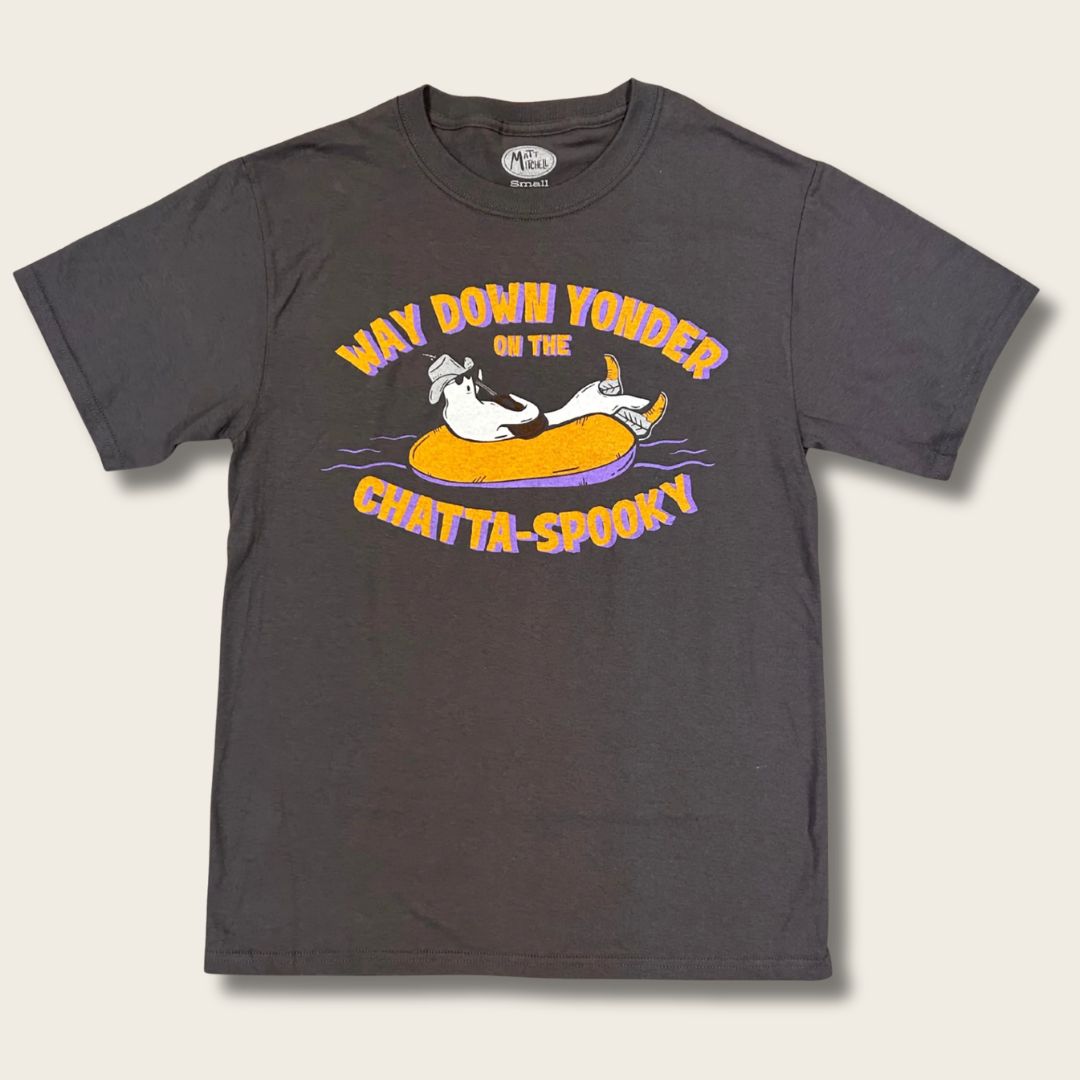 A dark charcoal gray short-sleeve t-shirt with a colorful graphic print of a cartoon cat lounging in an orange inner tube, with the text 'WAY DOWN YONDER ON THE CHATTA-SPOOKY'.